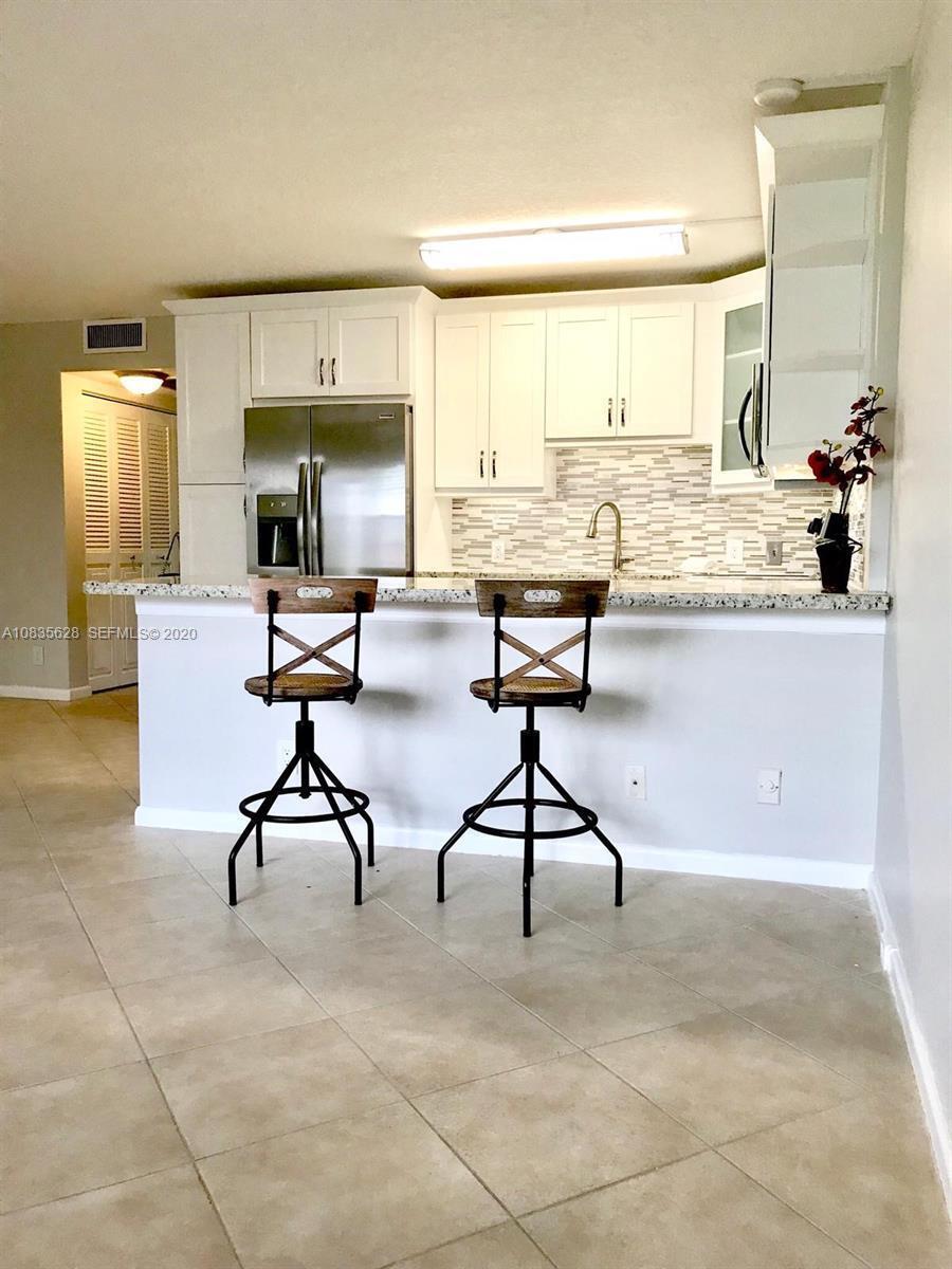 A kitchen features white cabinets, stainless steel appliances, a tiled backsplash, and two bar stools — 86 Mansfield C, Boca Raton FL 33434, BOCA RATON, FL