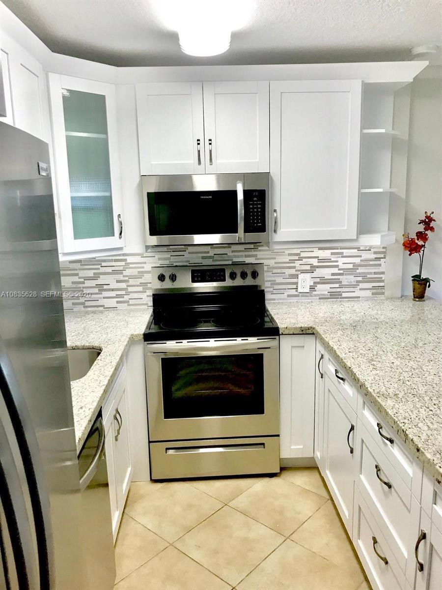 A kitchen features white cabinets, stainless steel appliances, granite countertops, and a tiled backsplash — 86 Mansfield C, Boca Raton FL 33434, BOCA RATON, FL