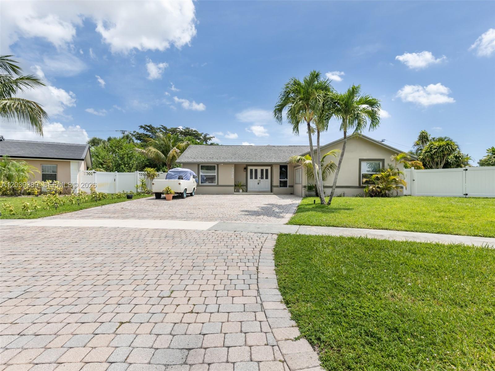 A single-story house with a paved driveway, palm trees, and a white fence — 19323 Carolina Cir, Boca Raton FL 33434, BOCA RATON, FL