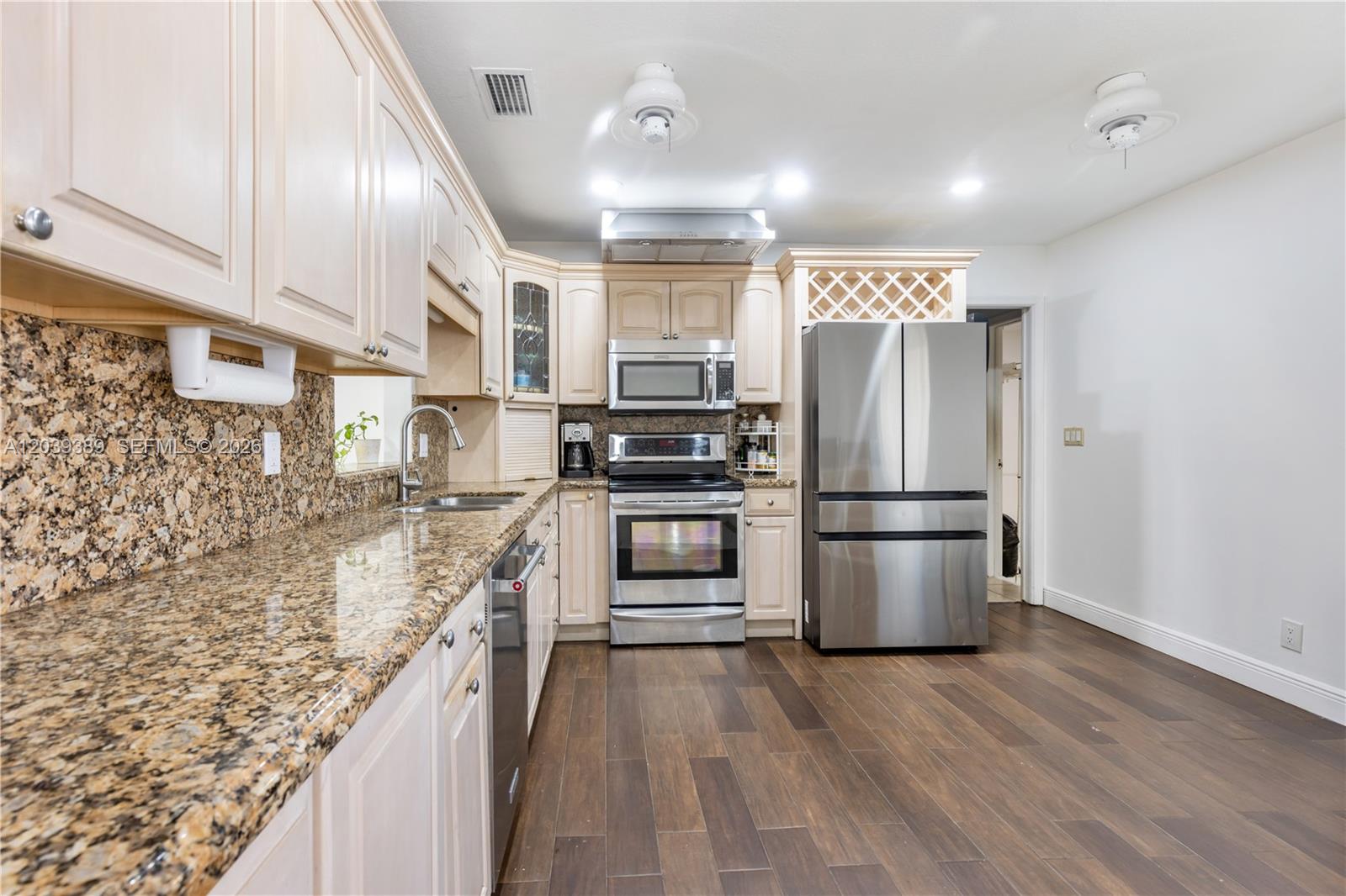 A kitchen features light wood cabinets, granite countertops, stainless steel appliances, and dark wood flooring — 19323 Carolina Cir, Boca Raton FL 33434, BOCA RATON, FL