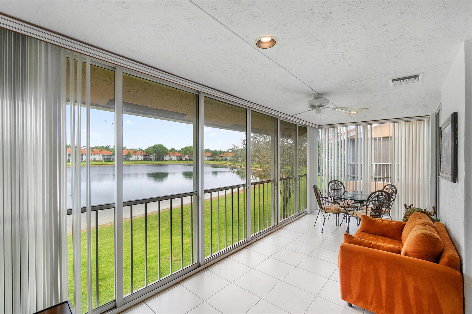 A sunroom with white tile floors, an orange sofa, and a view of a lake — 9829 Seacrest Circle # 202, Boynton Beach FL 33437, BOYNTON BEACH, FL