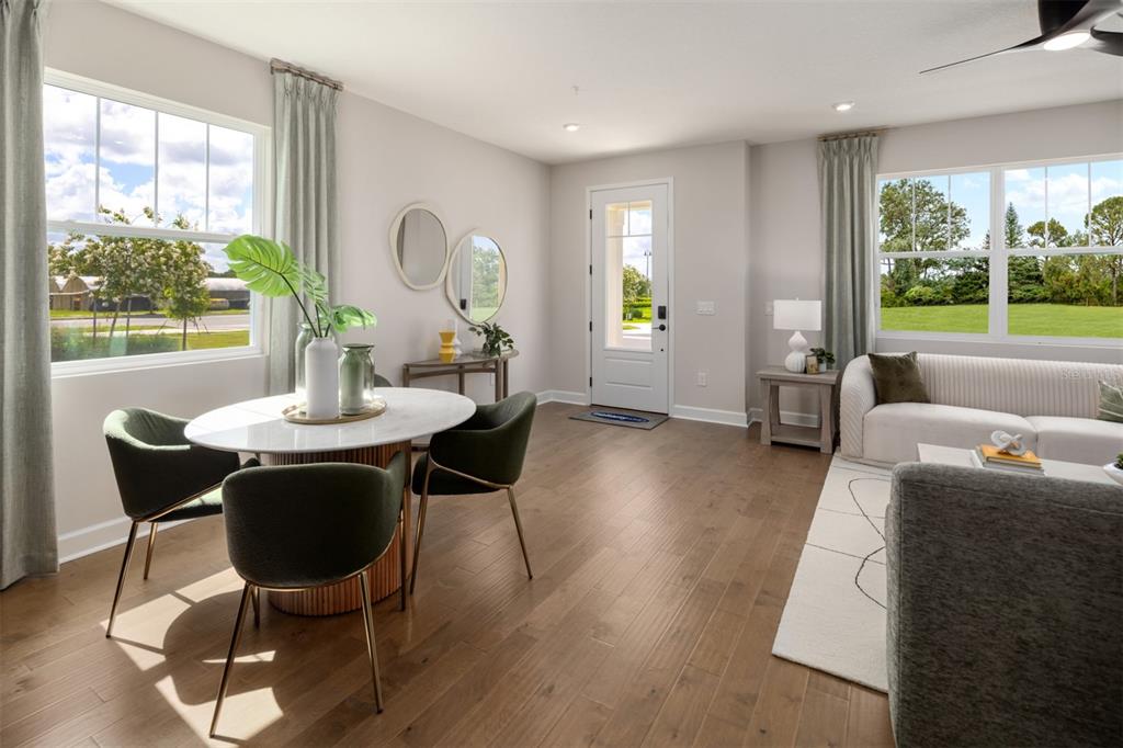 A bright living and dining area features light wood flooring, large windows, and modern furniture — 2832 CAMELLIA FLOWER STREET, APOPKA, FL