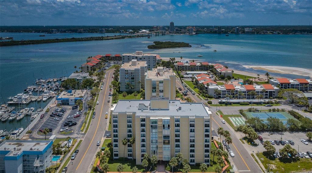 An aerial view shows multi-story apartment buildings, a marina, and a bridge over the water — 851 BAYWAY BOULEVARD UNIT 101, CLEARWATER BEACH, FL