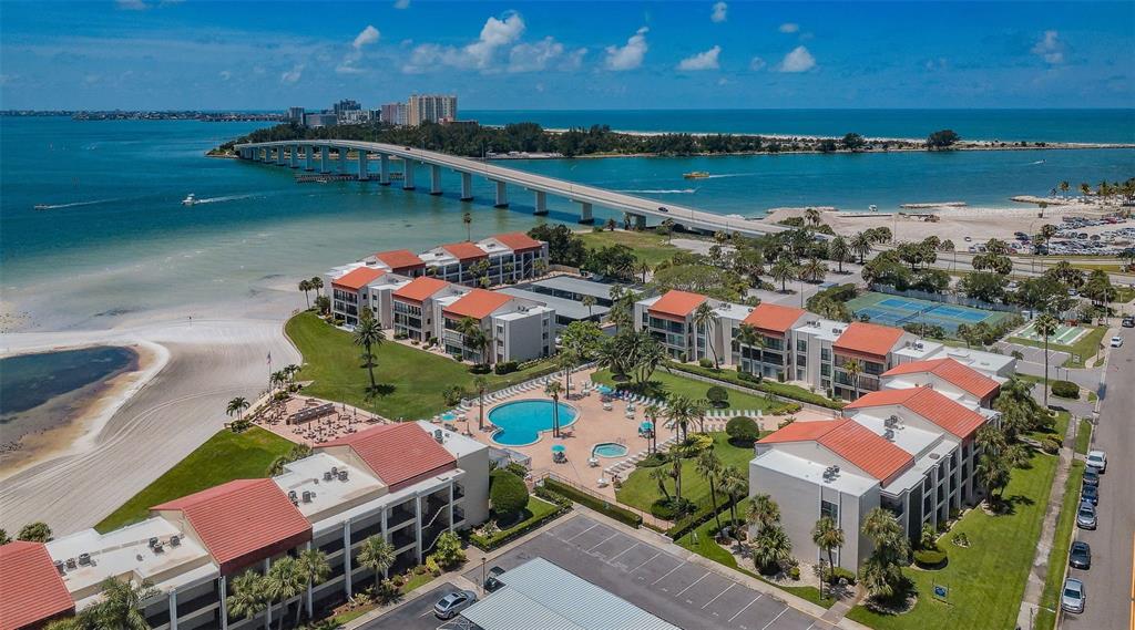 An aerial view shows a multi-story apartment complex with a pool near a coastal bridge — 851 BAYWAY BOULEVARD UNIT 101, CLEARWATER BEACH, FL