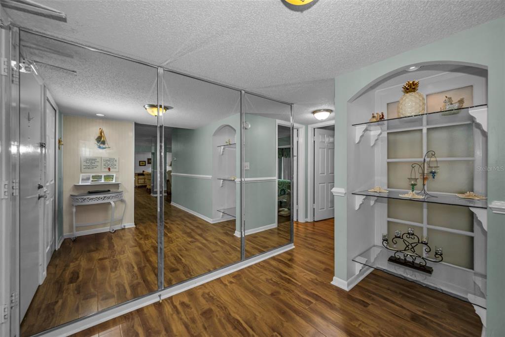 A hallway features wood-look flooring, mirrored closet doors, and a built-in arched display niche — 851 BAYWAY BOULEVARD UNIT 101, CLEARWATER BEACH, FL