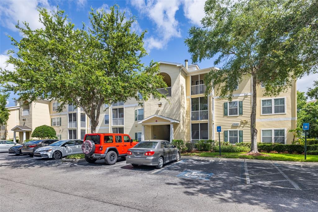 A multi-story apartment building with yellow siding and a parking lot in the foreground — 18439 BRIDLE CLUB DRIVE, TAMPA, FL