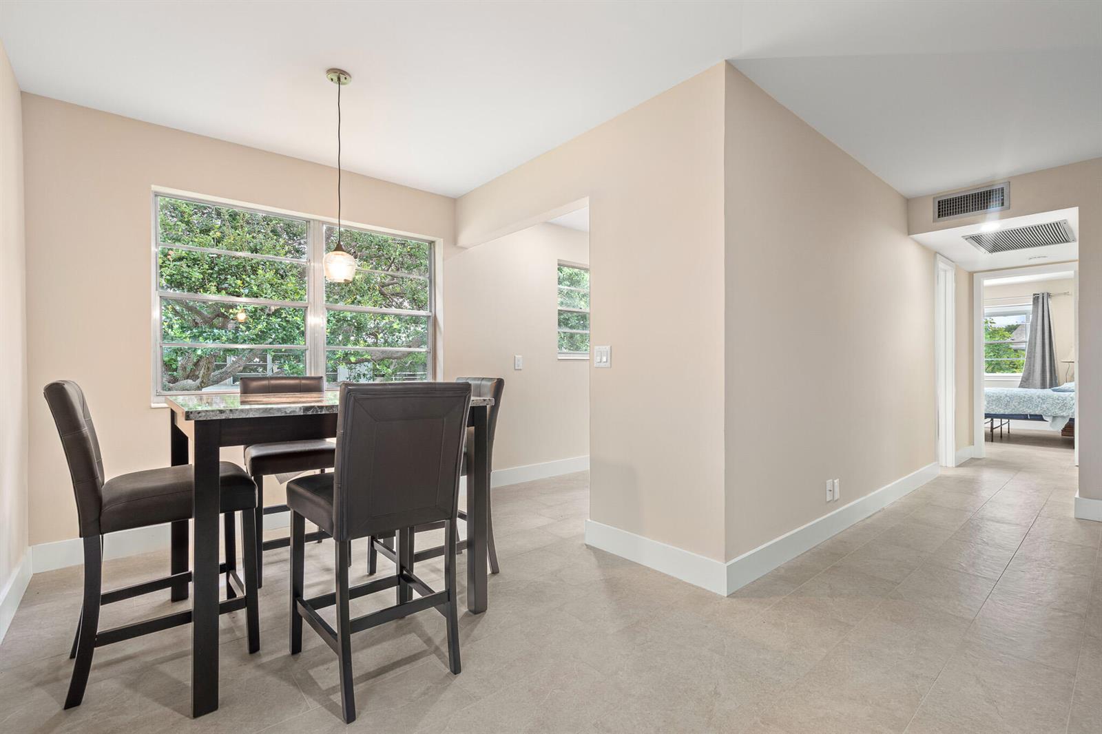 A dining area with a high-top table and chairs sits beside a hallway leading to a bedroom — 168 Farnham, Deerfield Beach FL 33442, DEERFIELD BEACH, FL