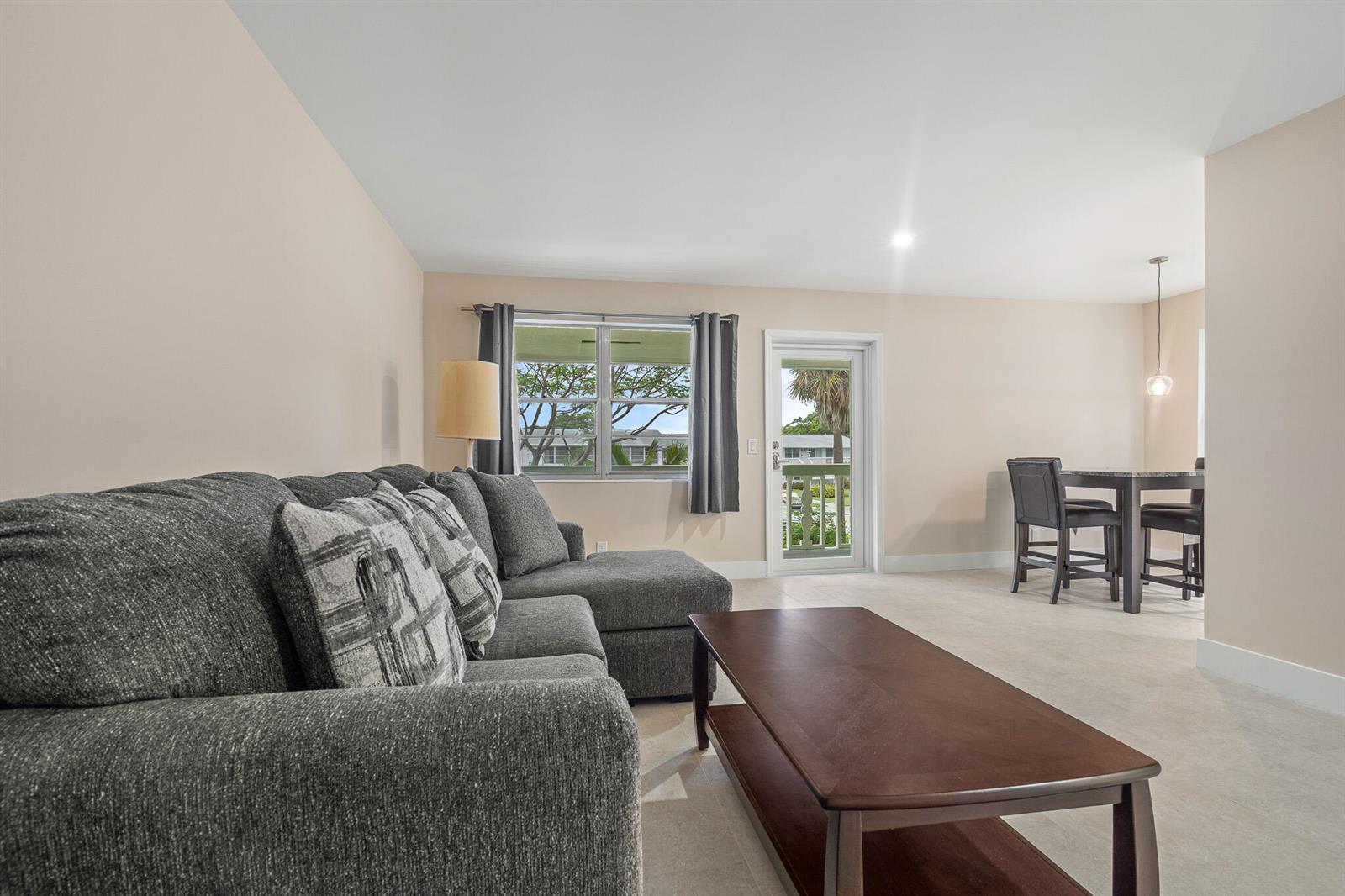 A living room with a gray sectional sofa, coffee table, and adjacent dining area — 168 Farnham, Deerfield Beach FL 33442, DEERFIELD BEACH, FL