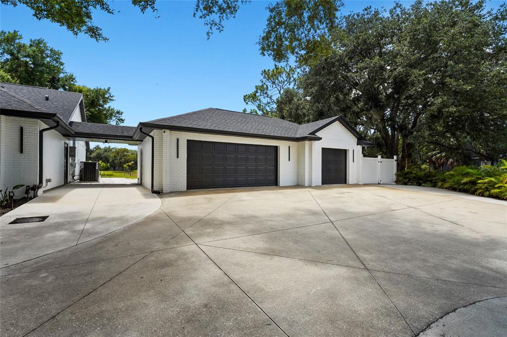 A white brick garage with a black roof and doors sits beside a concrete driveway — 906 136TH STREET E, BRADENTON, FL