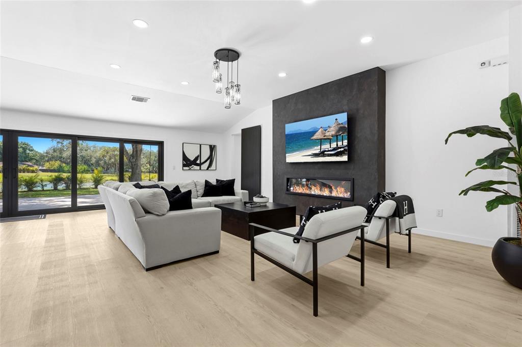 A modern living room features a dark fireplace wall, light wood floors, and large glass doors — 906 136TH STREET E, BRADENTON, FL