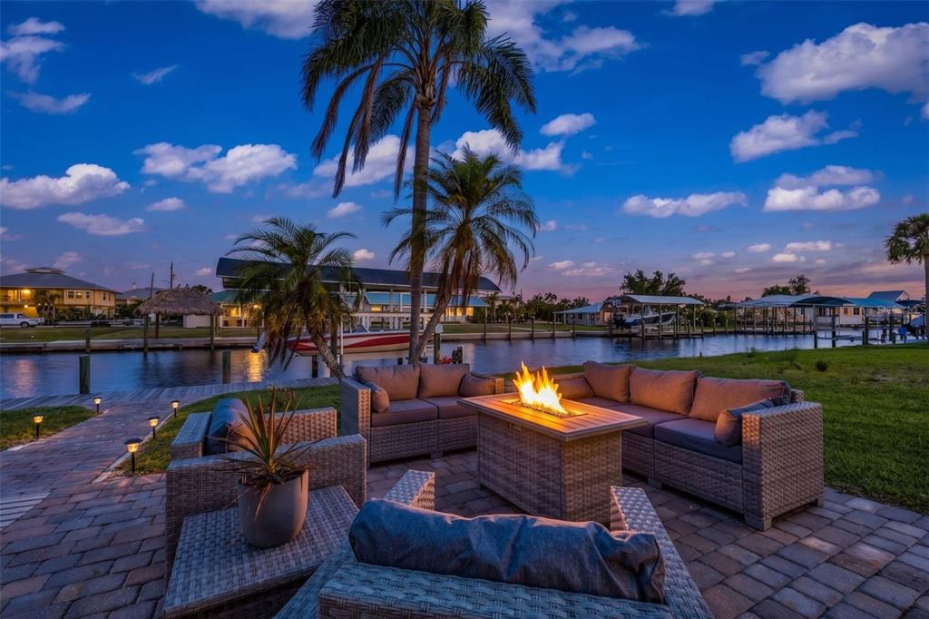 A patio with wicker furniture and a fire pit overlooks a canal at sunset — 24240 HENRY MORGAN BLVD, PUNTA GORDA, FL