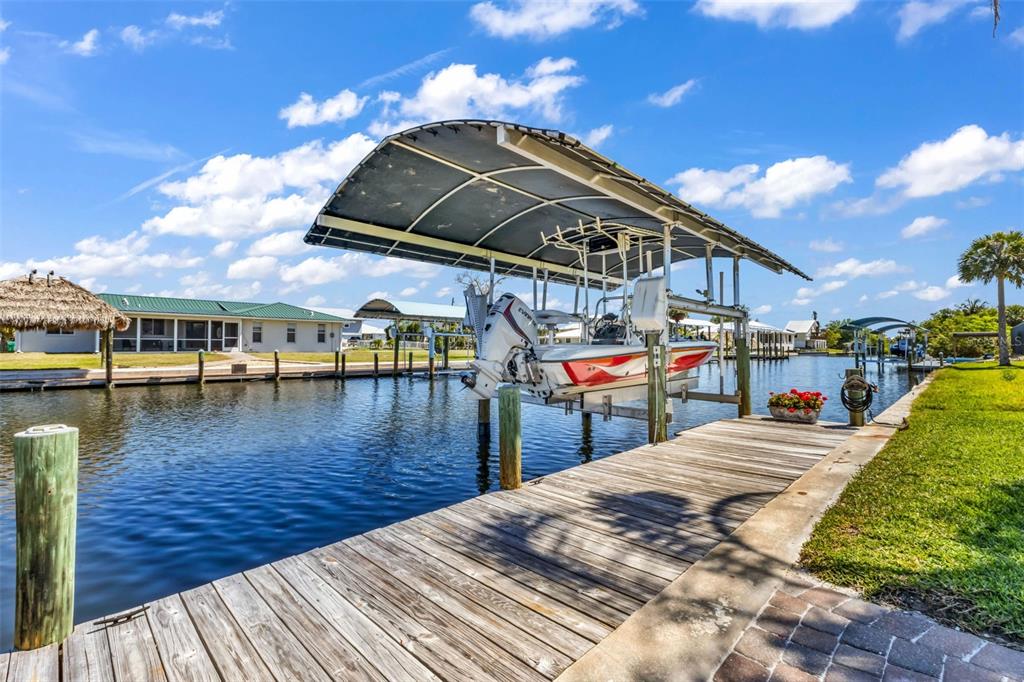 A boat on a lift sits under a canopy at a wooden dock on a canal — 24240 HENRY MORGAN BLVD, PUNTA GORDA, FL