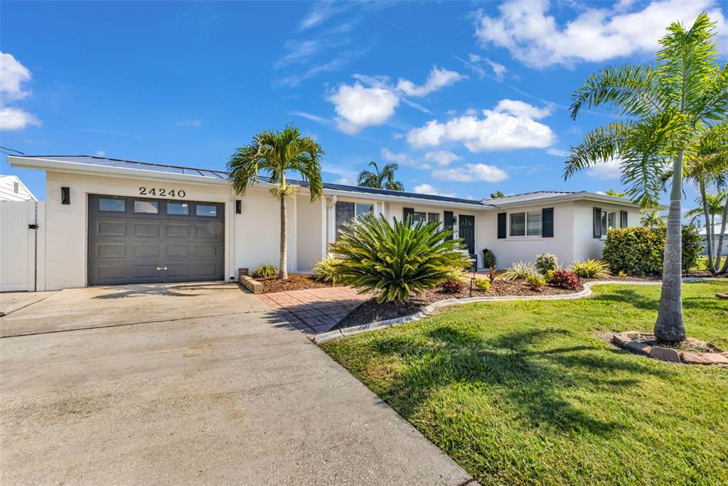 A single-story house with a white exterior, a gray garage door, and palm trees — 24240 HENRY MORGAN BLVD, PUNTA GORDA, FL
