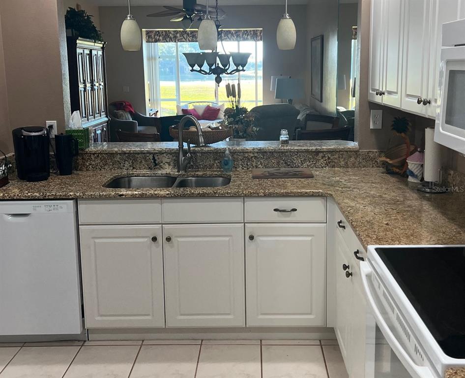 A kitchen features white cabinets, granite countertops, a stainless steel sink, and a pass-through window — 8750 OLDE HICKORY AVENUE UNIT 9105, SARASOTA, FL