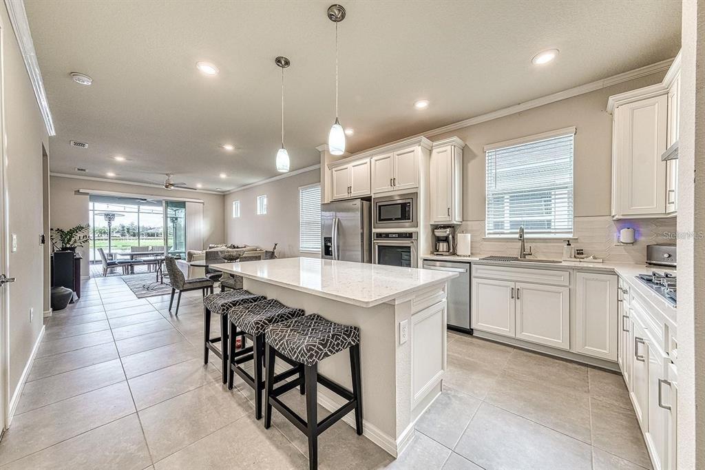A kitchen with white cabinets, a quartz-topped island, and tile flooring opens to a living area — 2505 CLIFF WAY, ST CLOUD, FL
