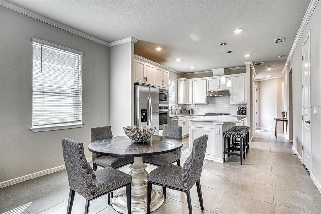 A dining area with a round table and chairs sits adjacent to a white kitchen — 2505 CLIFF WAY, ST CLOUD, FL