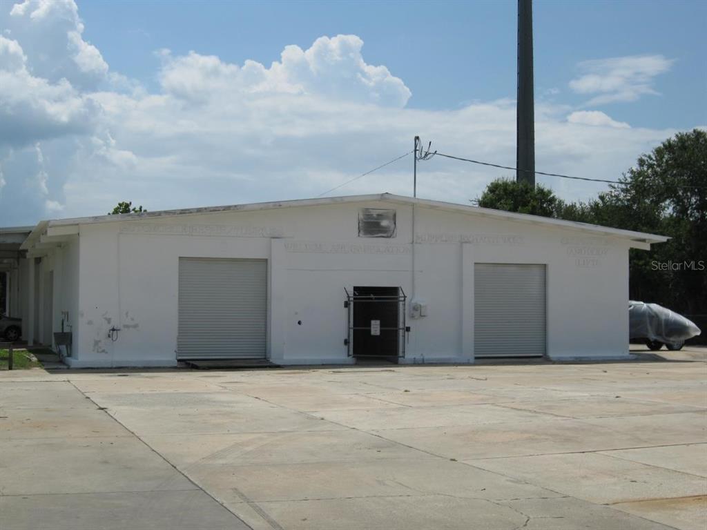 A white, single-story commercial building with two roll-up garage doors and a central entrance — 1200 S JOHN YOUNG PARKWAY, KISSIMMEE, FL
