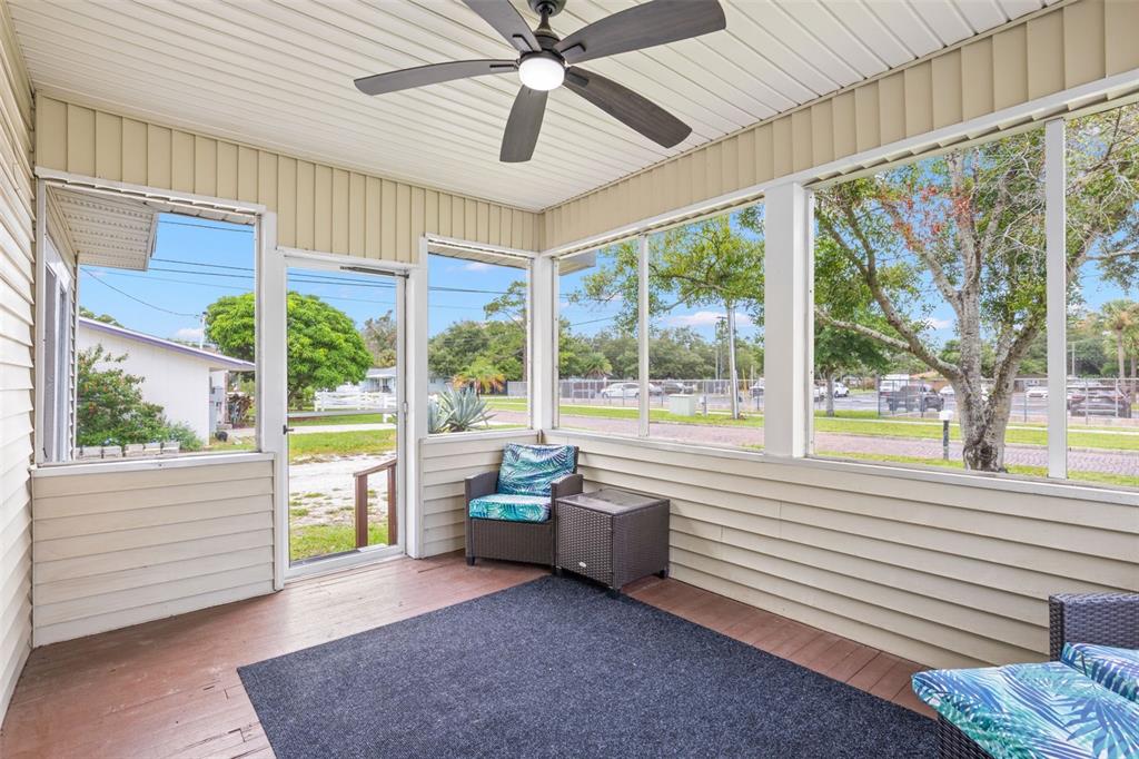 A screened-in porch features a ceiling fan, dark wicker furniture, and large windows overlooking trees — 605 3RD AVENUE SW, LARGO, FL