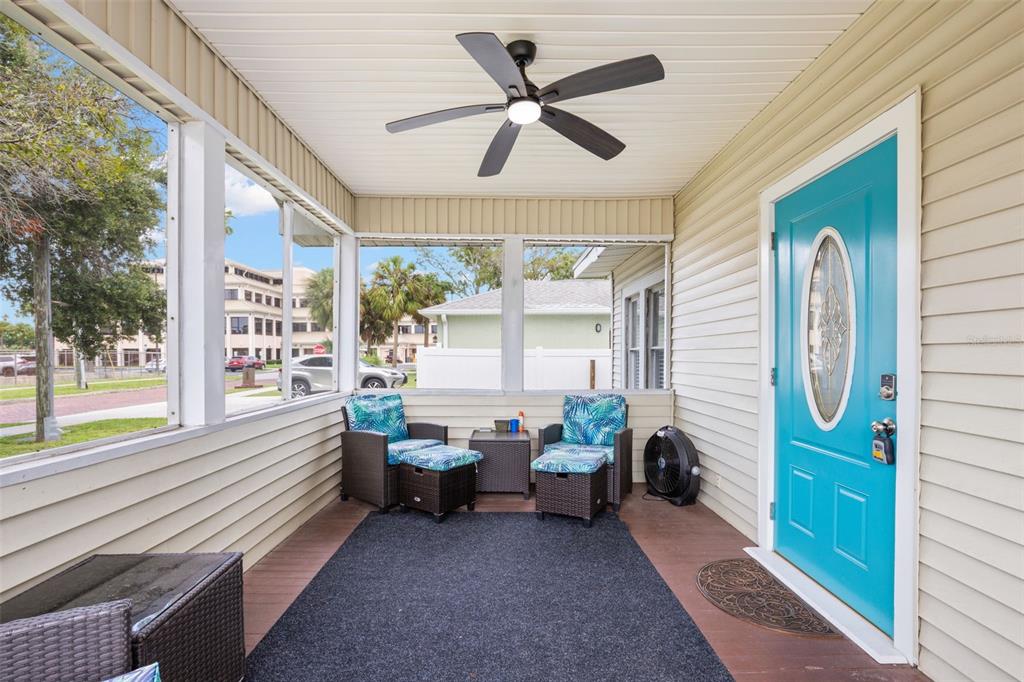 A screened-in porch features a bright blue front door, wicker furniture, and a ceiling fan — 605 3RD AVENUE SW, LARGO, FL