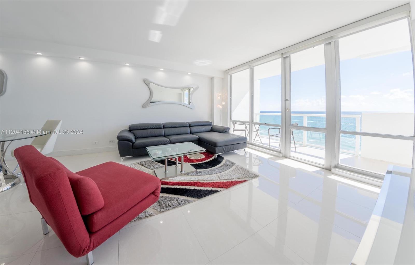 A modern living room features white tile floors, a dark sectional, and oceanfront balcony views — 5601 Collins Ave # 1603, Miami Beach FL 33140, MIAMI BEACH, FL