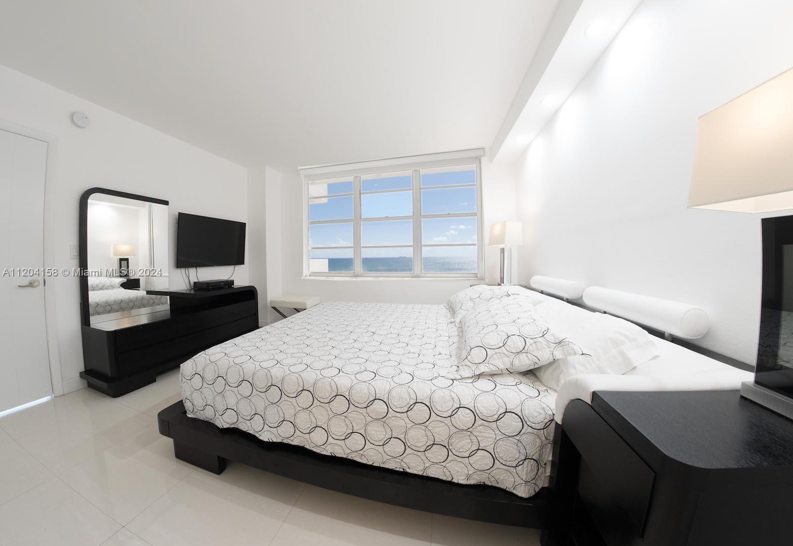 A modern bedroom features a black platform bed, matching dresser, and a view of the ocean — 5601 Collins Ave # 1603, Miami Beach FL 33140, MIAMI BEACH, FL