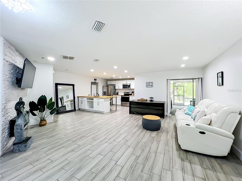 An open-concept living room and kitchen feature light wood-look tile floors and white cabinetry — 2425 LAUDERDALE COURT, ORLANDO, FL