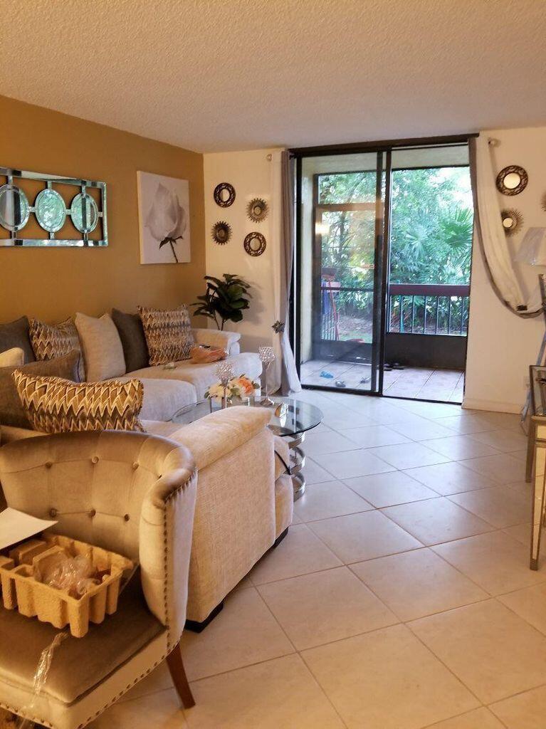 A living room features beige tile floors, a neutral sofa, and a sliding glass balcony door — 733 SE 1st Way # 105, Deerfield Beach FL 33441, DEERFIELD BEACH, FL