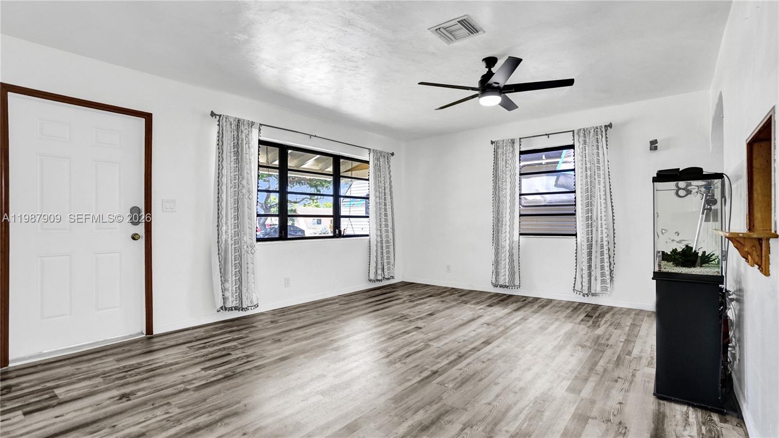 A living room features white walls, wood-look flooring, a ceiling fan, and two windows — 1007 N 31st Rd, Hollywood FL 33021, HOLLYWOOD, FL