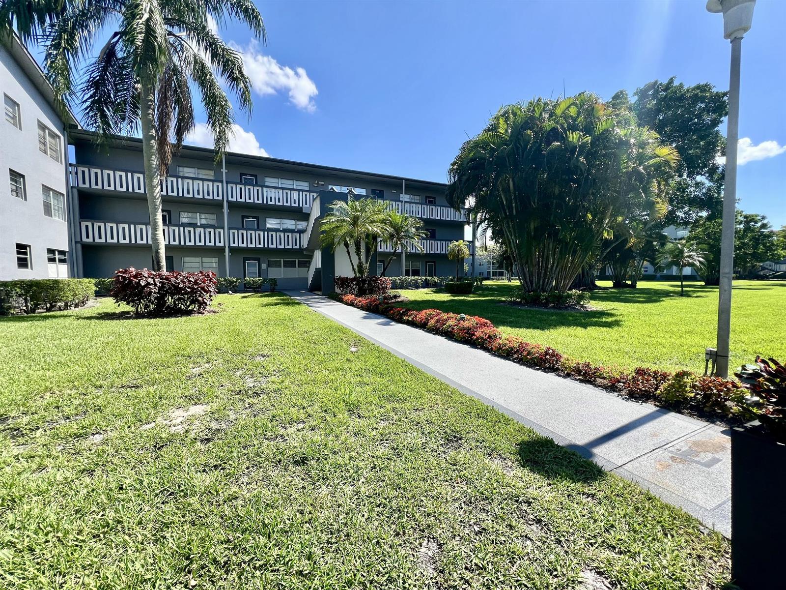 A multi-story apartment building with a concrete walkway leading to the entrance — 209 Suffolk E, Boca Raton FL 33434, BOCA RATON, FL
