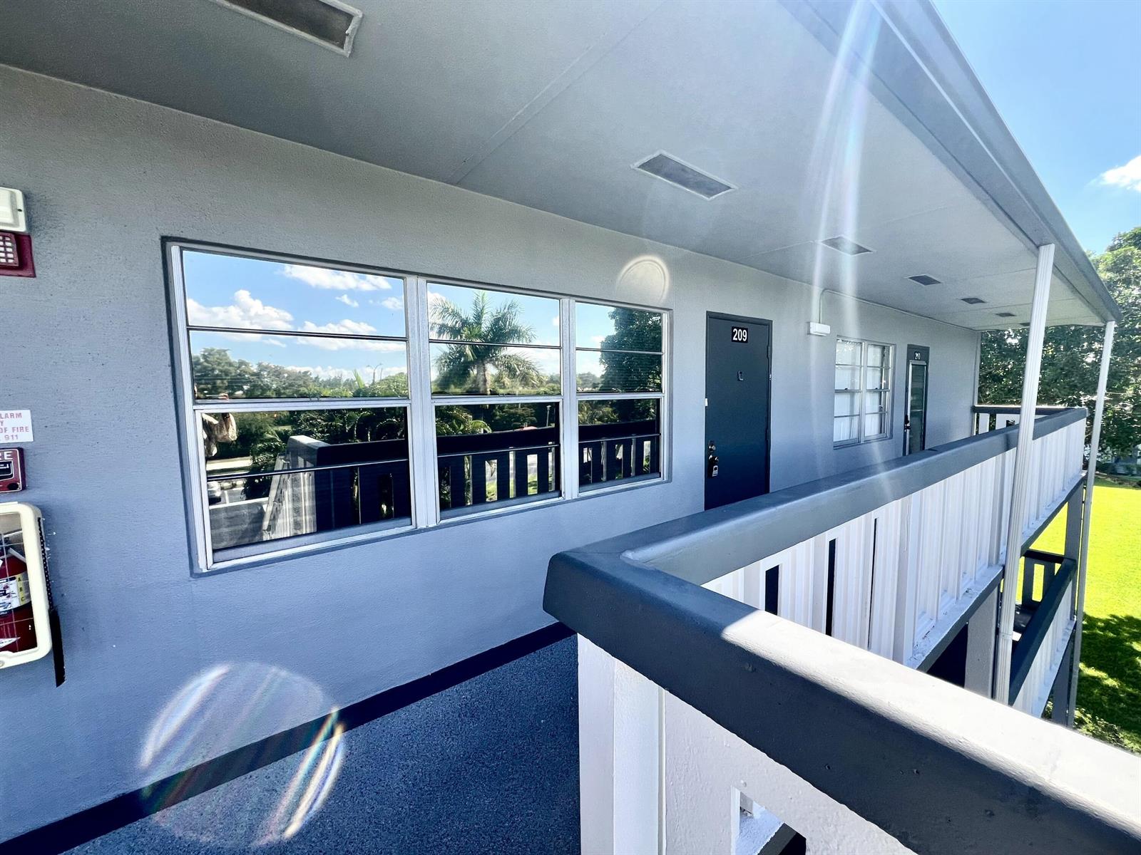 An exterior walkway with a fire extinguisher, a door numbered 209, and a metal railing — 209 Suffolk E, Boca Raton FL 33434, BOCA RATON, FL