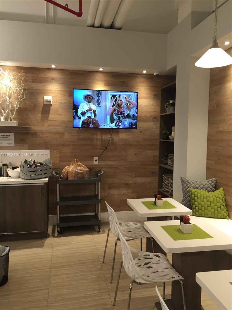 A dining area features wood-paneled walls, a wall-mounted television, and white tables with chairs — 10275 Collins Ave # 1402, Bal Harbour FL 33154, BAL HARBOUR, FL