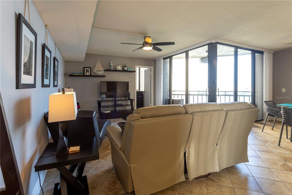 A living room features a beige sofa, a television, and large windows overlooking a balcony — 5825 PUERTA DEL SOL BOULEVARD S UNIT 265, ST PETERSBURG, FL