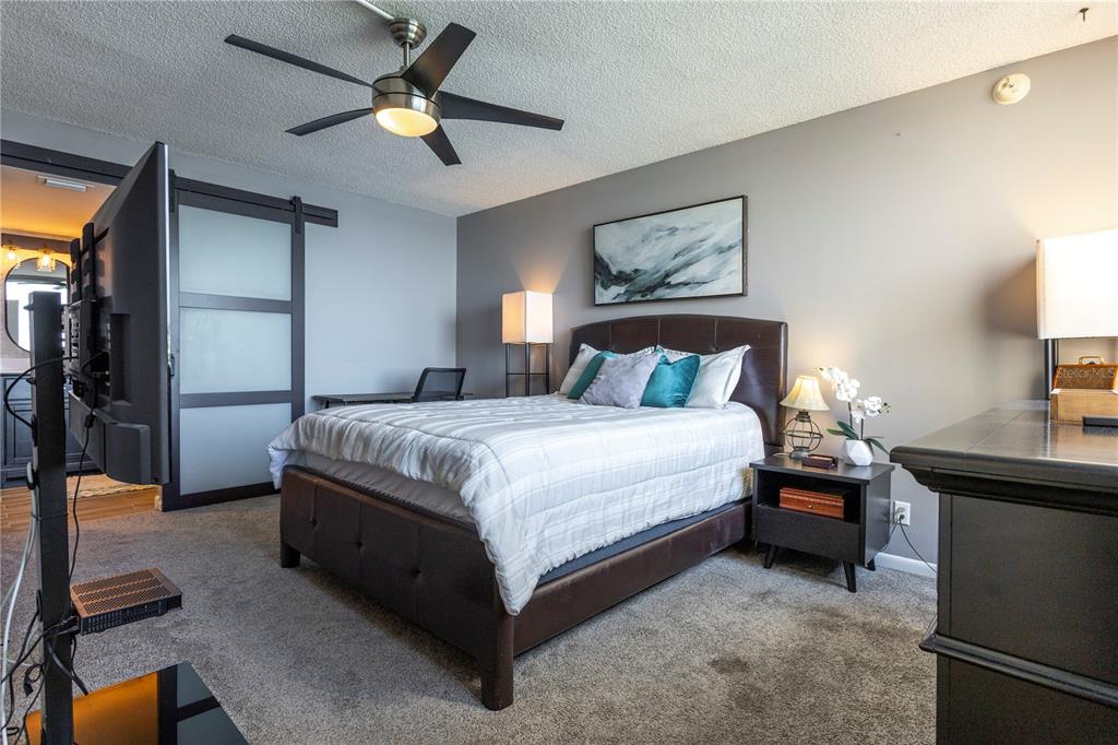 A bedroom features a brown upholstered bed, a ceiling fan, and a sliding barn door — 5825 PUERTA DEL SOL BOULEVARD S UNIT 265, ST PETERSBURG, FL