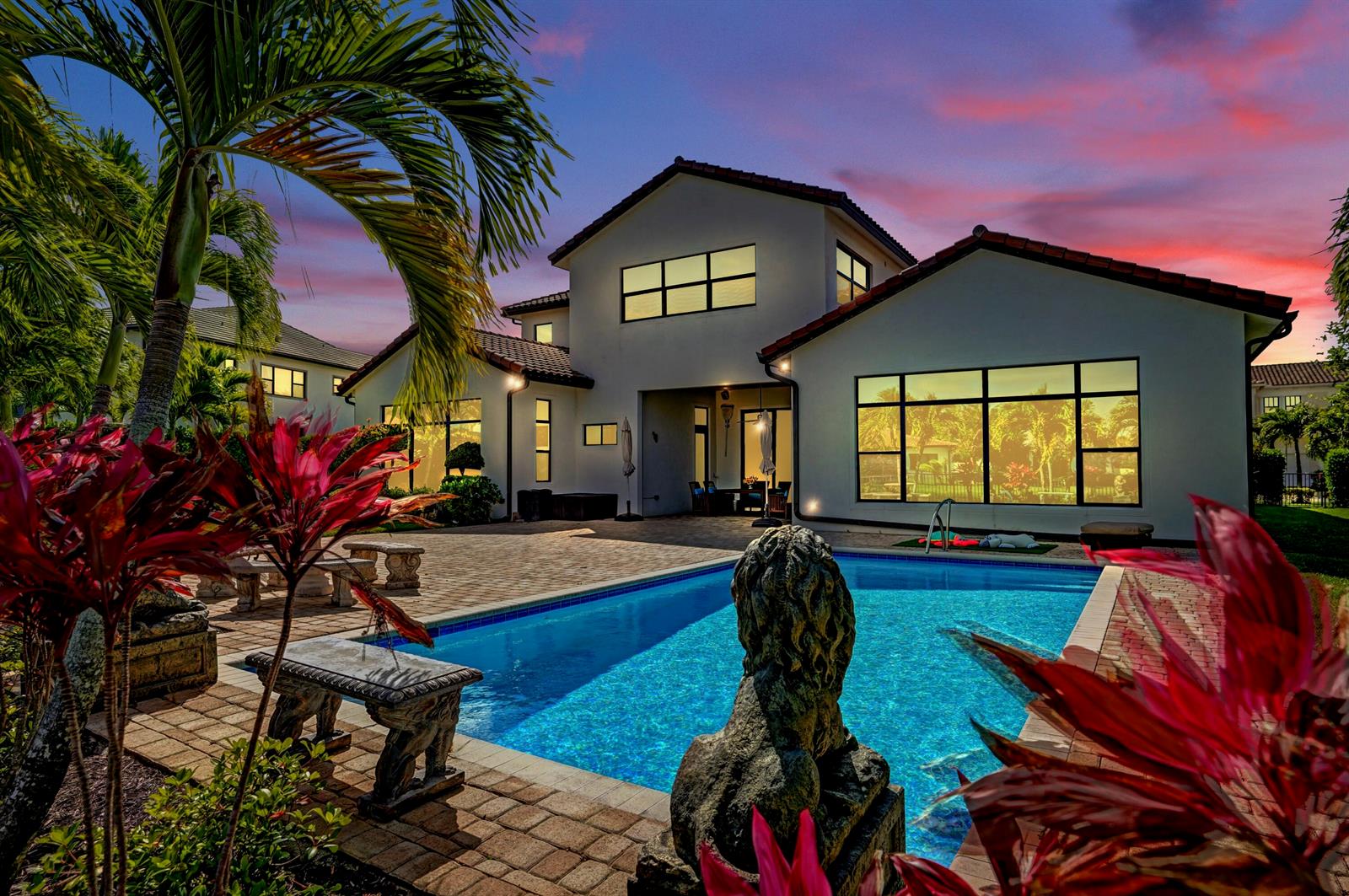A two-story house with a swimming pool, stone patio, and palm trees at sunset — 9420 Grand Prix Lane, Boynton Beach FL 33472, BOYNTON BEACH, FL