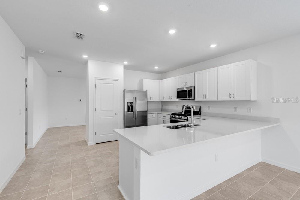 An empty room with gray tile flooring and a window, leading to an open kitchen — 12449 WHISK COURT, HUDSON, FL