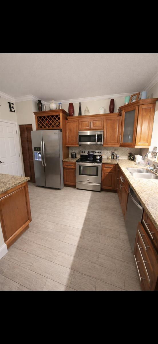 A kitchen with wood cabinets, stainless steel appliances, granite countertops, and light wood-look tile flooring — 223 Foxtail Drive # C, FL 33415, FL