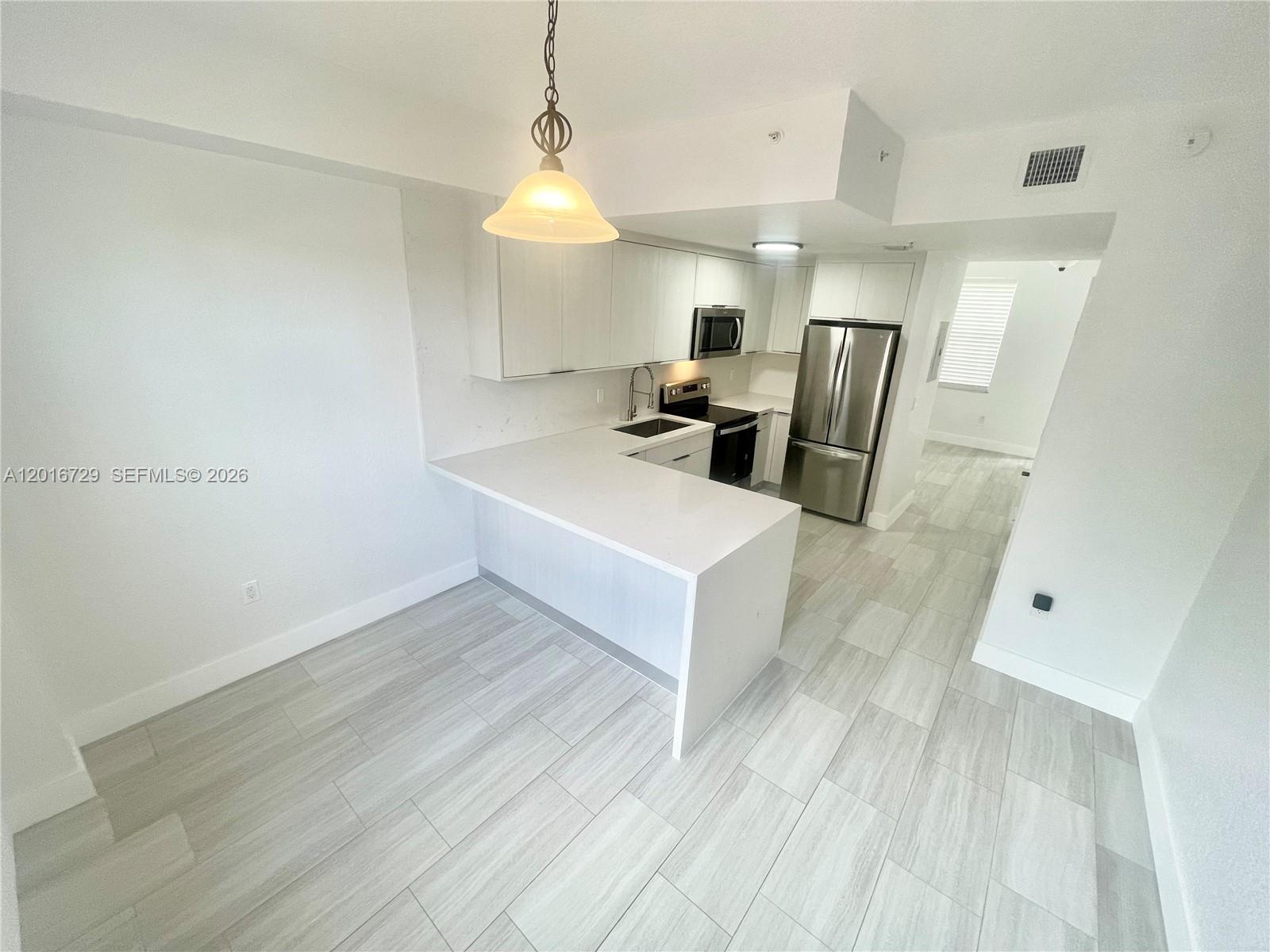A modern kitchen features white cabinets, stainless steel appliances, and light-colored tile flooring — 77 E 4th St # A212, Hialeah FL 33010, HIALEAH, FL