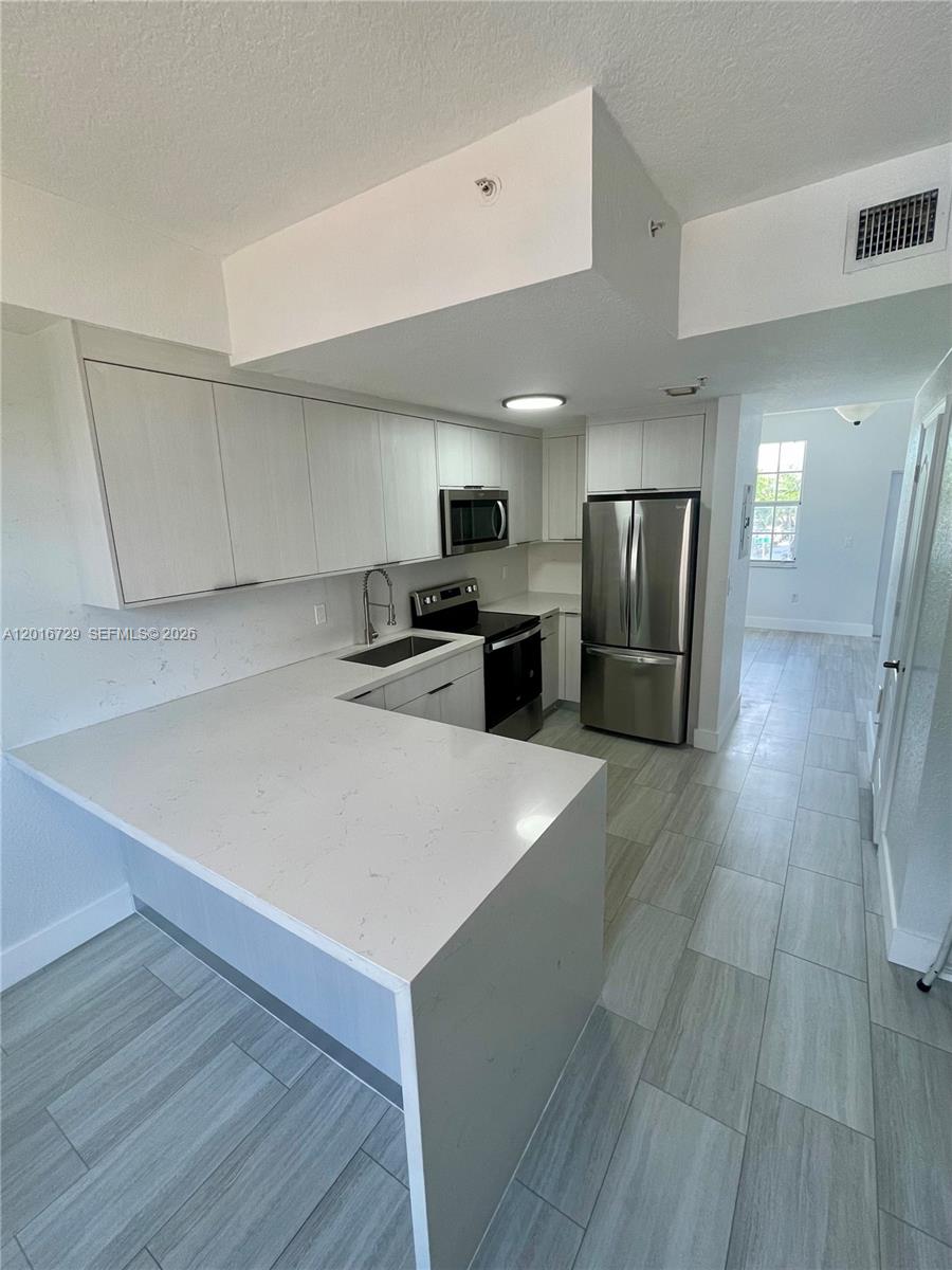 An empty room features white walls, light wood-look tile flooring, two windows, and a door — 77 E 4th St # A212, Hialeah FL 33010, HIALEAH, FL