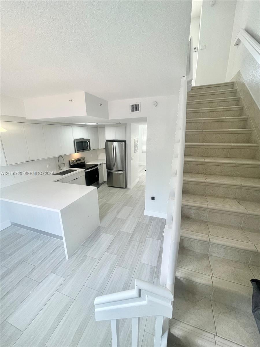 An empty room features light-colored wood-look tile flooring, white walls, two windows, and a balcony — 77 E 4th St # A212, Hialeah FL 33010, HIALEAH, FL