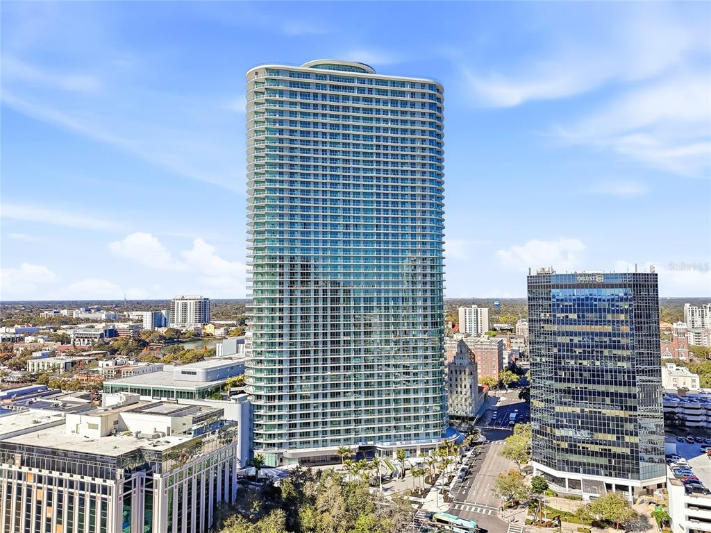An aerial view shows a tall, modern glass residential tower next to a dark office building — 400 CENTRAL AVENUE UNIT 505, ST PETERSBURG, FL