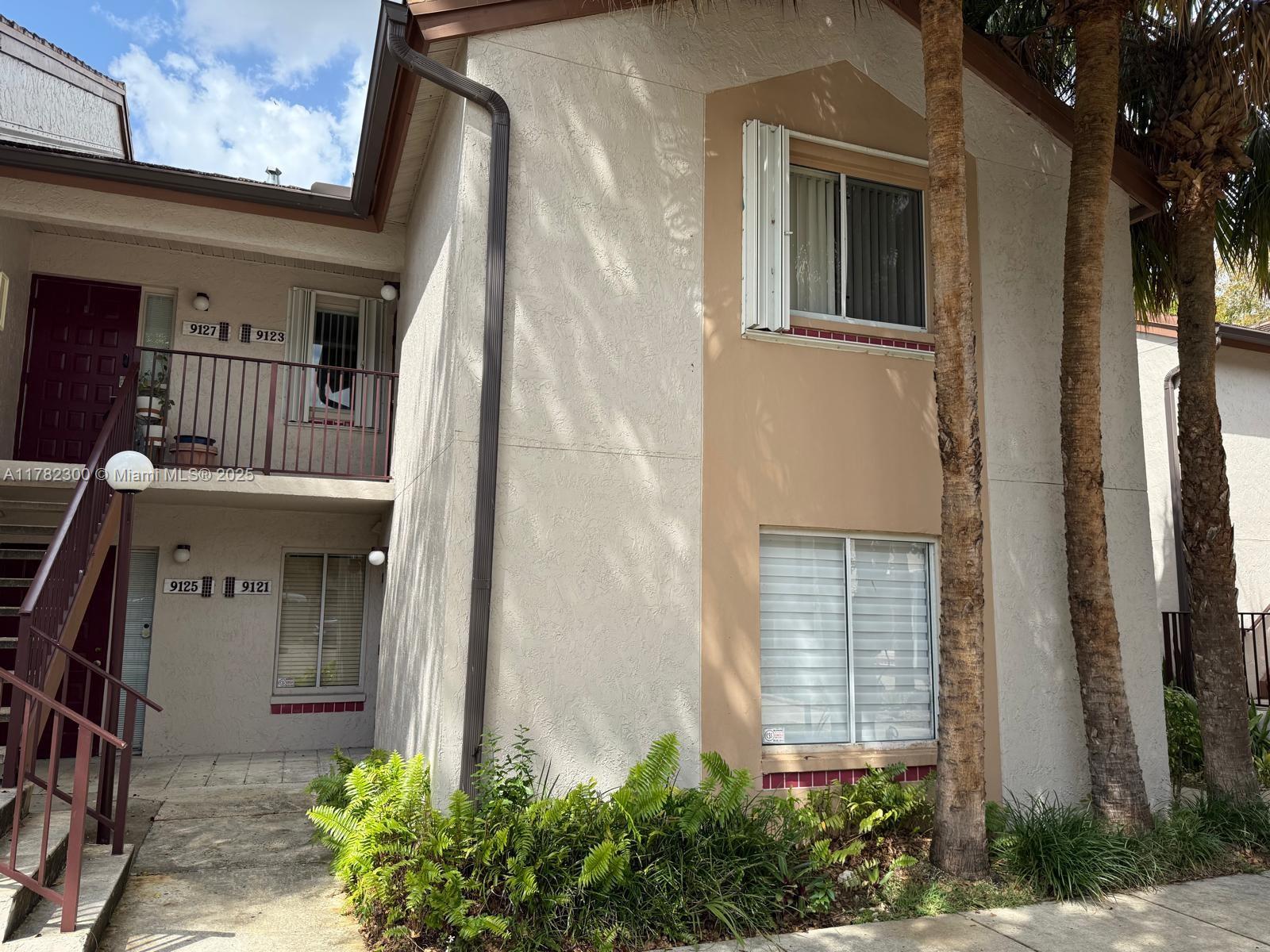 The exterior of a two-story apartment building features beige stucco walls and a metal staircase — 9121 SW 138th Pl # 9121, Miami FL 33186, MIAMI, FL