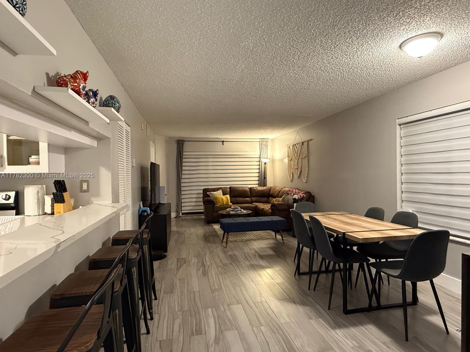 An open-concept living and dining area features wood-look tile flooring and a breakfast bar — 9121 SW 138th Pl # 9121, Miami FL 33186, MIAMI, FL