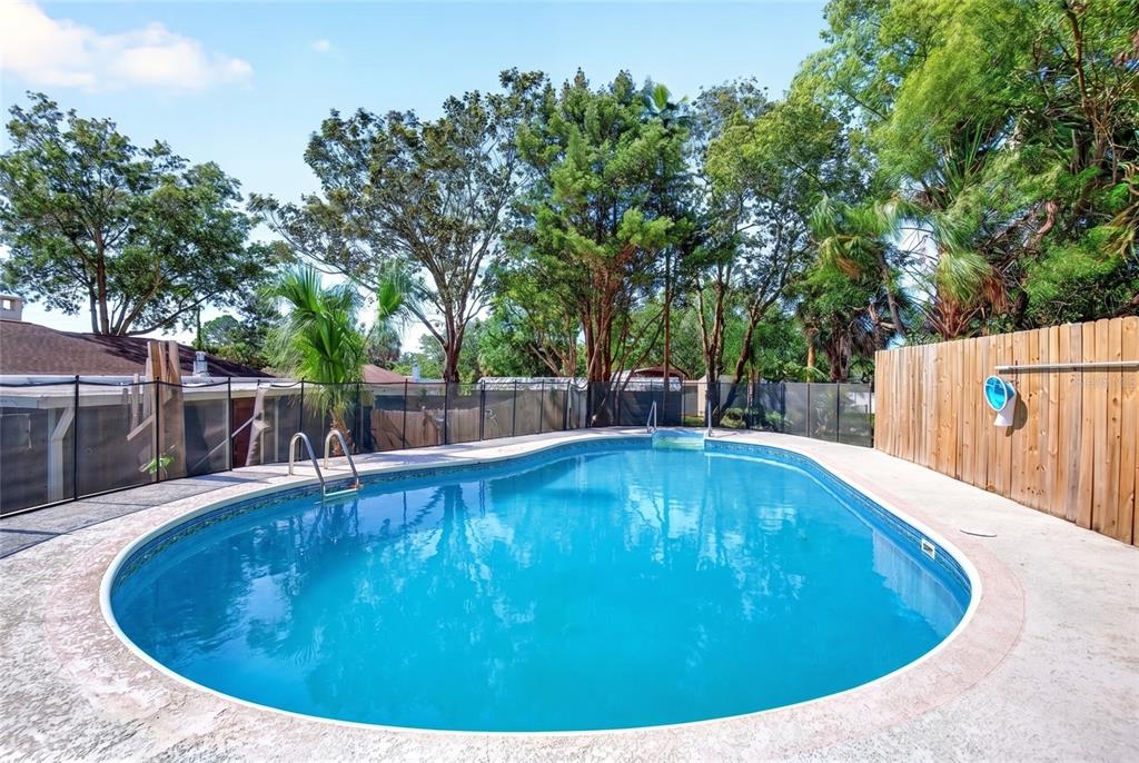 An outdoor swimming pool surrounded by a black mesh safety fence and a wooden fence — 16206 SEA PINES DRIVE, HUDSON, FL