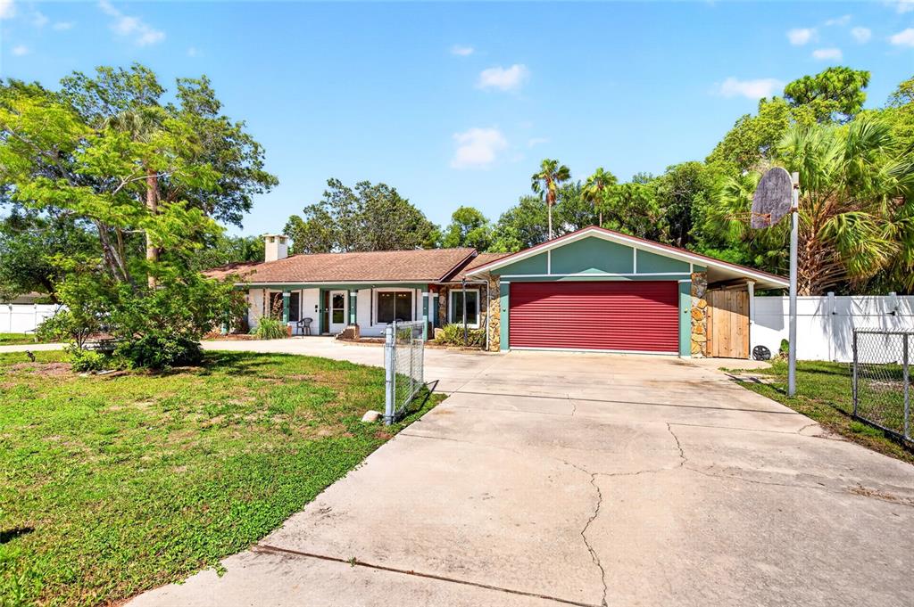 A single-story house with a red garage door, a concrete driveway, and surrounding trees — 16206 SEA PINES DRIVE, HUDSON, FL