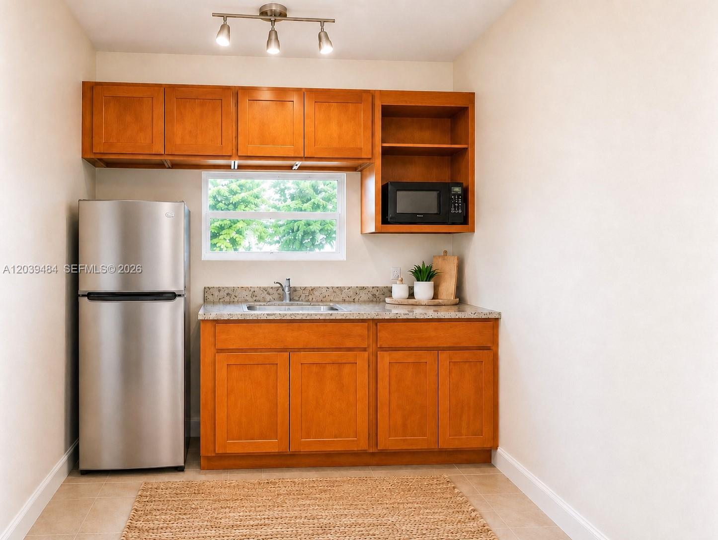A small kitchen features wooden cabinets, a stainless steel refrigerator, and a granite countertop — 223 NW 12th St # 4, Miami FL 33136, MIAMI, FL
