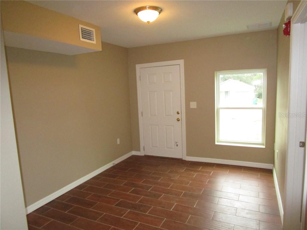 An empty room features tan walls, a white door, a window, and wood-look tile flooring — 1002 E MCDONALD AVENUE UNIT 4, EUSTIS, FL