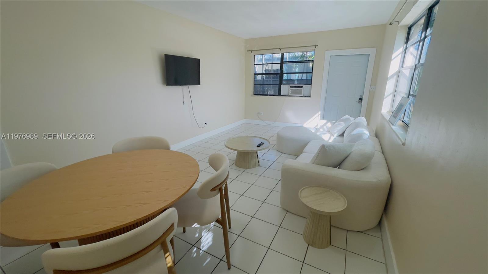 A living and dining area features white tile floors, a white sofa, and a round table — 807 86th St # 801, Miami Beach FL 33141, MIAMI BEACH, FL
