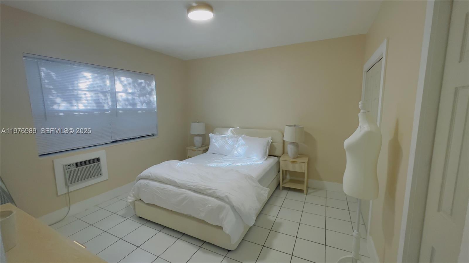 A bedroom features white tile flooring, a bed with white bedding, and a window unit — 807 86th St # 801, Miami Beach FL 33141, MIAMI BEACH, FL