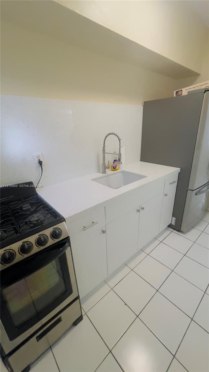 A kitchen features white cabinets, a white countertop, a sink, and a stainless steel stove — 807 86th St # 801, Miami Beach FL 33141, MIAMI BEACH, FL