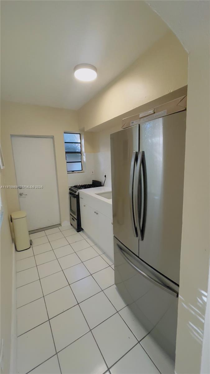 A narrow kitchen features white cabinets, a stainless steel refrigerator, and white tile flooring — 807 86th St # 801, Miami Beach FL 33141, MIAMI BEACH, FL
